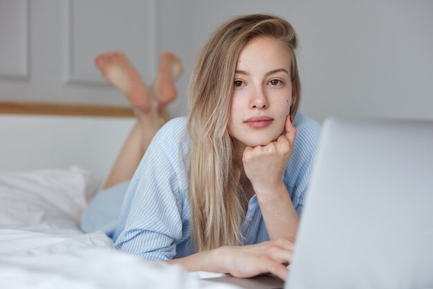 Bella giovane donna che si distende a letto con il computer portatile