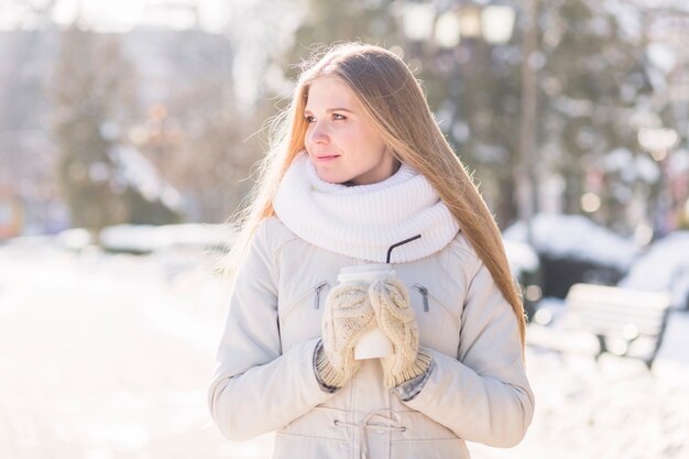 Bella giovane donna che tiene caffè eliminabile in inverno