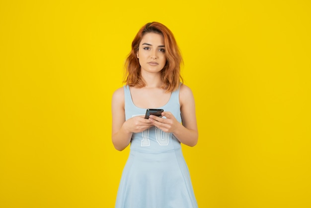 Bella giovane donna che tiene telefono e che guarda l'obbiettivo su giallo.