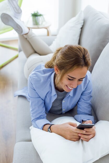 Bella giovane donna che utilizza il suo cellulare in casa.