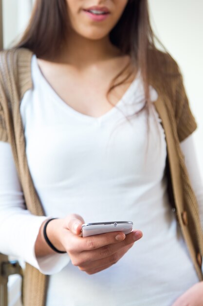 Bella giovane donna che utilizza il suo cellulare in casa.