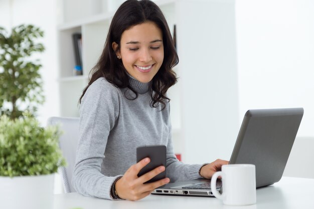 Bella giovane donna che utilizza il suo cellulare in casa.