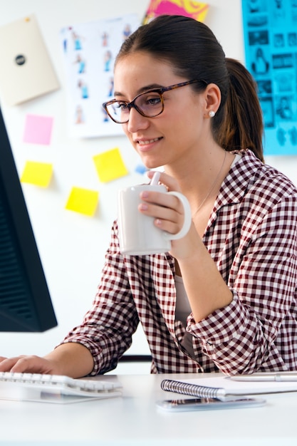 Bella giovane donna che utilizza il suo computer portatile in ufficio.