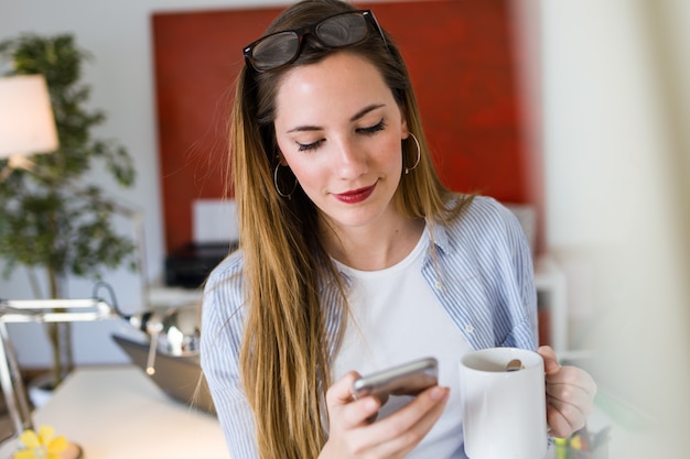 Bella giovane donna che utilizza il suo telefono cellulare in ufficio.