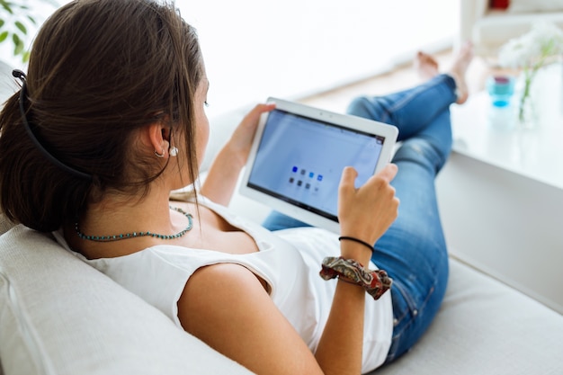 Bella giovane donna che utilizza la sua compressa digitale a casa.