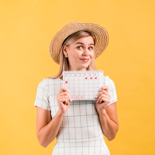 Bella giovane donna con cappello mostrando il calendario dell'ovulazione