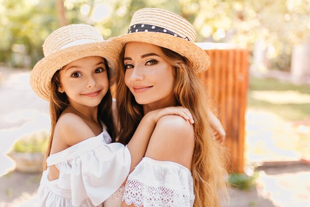 Bella giovane donna con grandi occhi verdi tenendo la figlia guardando con espressione del viso sorpreso. Foto all'aperto del primo piano della bella signora che trasporta il bambino intorno al parco soleggiato.