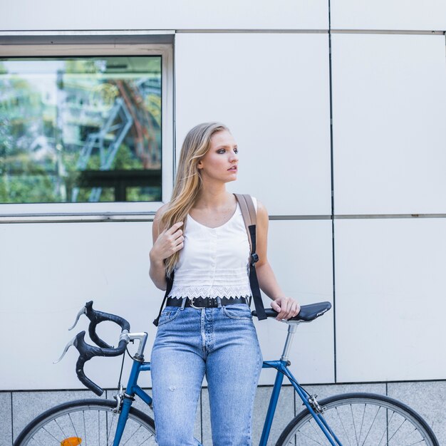 Bella giovane donna con il suo zaino che si appoggia sulla bicicletta