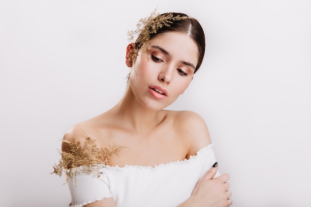 Bella giovane donna con labbra sensuali, guardando in basso con imbarazzo. Pose castane dalla pelle sane con belle piante tra i capelli e la parte superiore bianca.