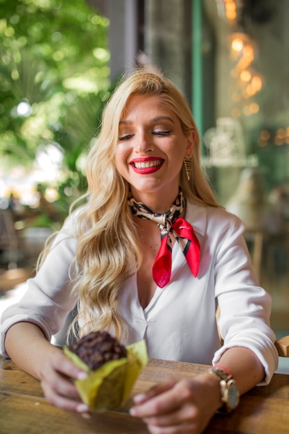 Bella giovane donna con lunghi capelli biondi tenendo delizioso muffin al cioccolato in mano