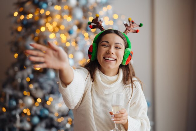 Bella giovane donna con un bicchiere di champagne a casa. Celebrazione di Natale