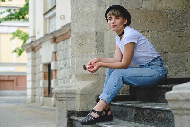 Bella giovane donna dei pantaloni a vita bassa che posa seduta sulle scale