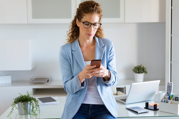 Bella giovane donna di affari che utilizza il suo telefono cellulare nell&#39;ufficio.