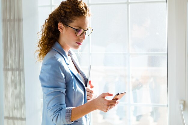 Bella giovane donna di affari che utilizza il suo telefono cellulare nell&#39;ufficio.