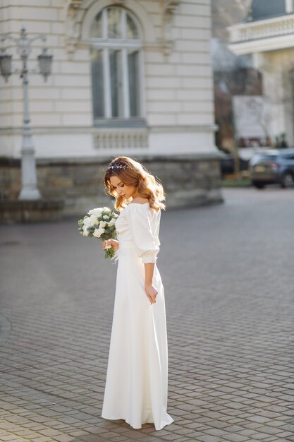 Bella giovane donna in abito da sposa in posa sulla strada in città