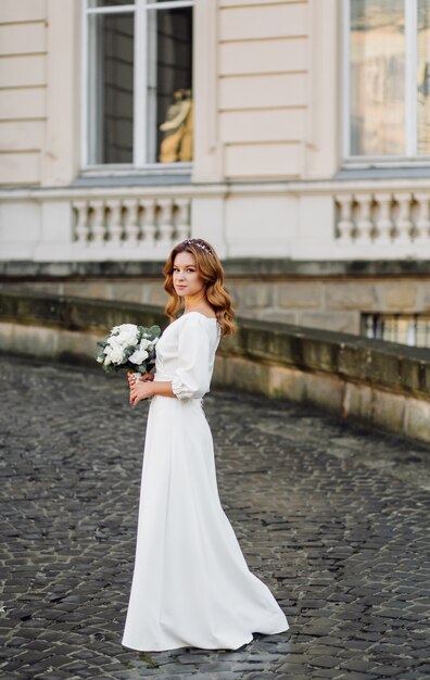 Bella giovane donna in abito da sposa in posa sulla strada in città