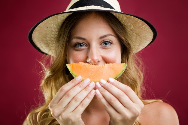 Bella giovane donna in bikini mangiare melone. Isolato su rosso.