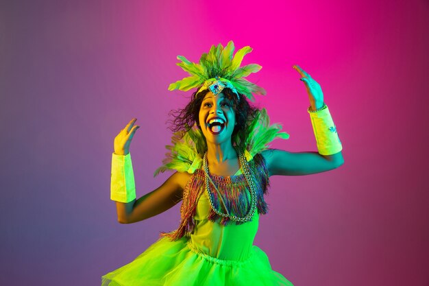 Bella giovane donna in costume di carnevale e mascherata su sfondo sfumato in studio con luce al neon