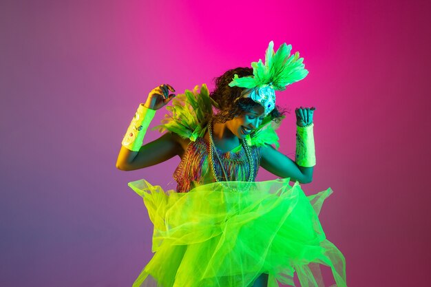 Bella giovane donna in costume di carnevale e mascherata su sfondo sfumato in studio con luce al neon