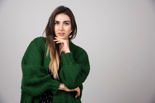 Bella giovane donna in maglione verde che propone alla macchina fotografica.