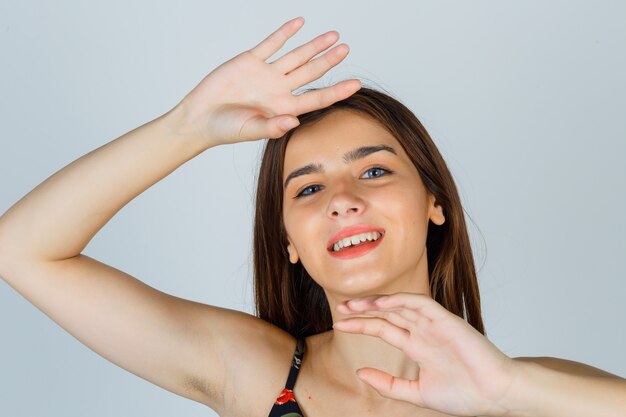 Bella giovane donna in posa con le mani intorno alla testa in camicetta e guardando allegro