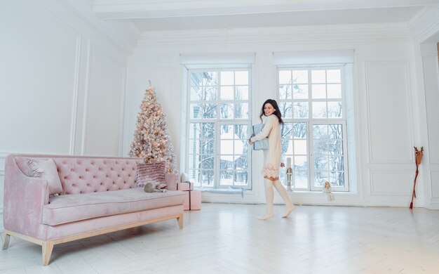 Bella giovane donna in vestito bianco che posa con il contenitore di regalo