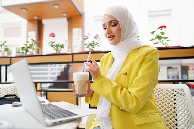 Bella giovane donna musulmana che usa il computer portatile mentre è seduta al bar