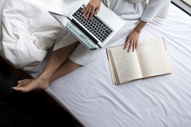 Bella giovane donna nel suo letto mentre controlla il suo computer portatile a casa.