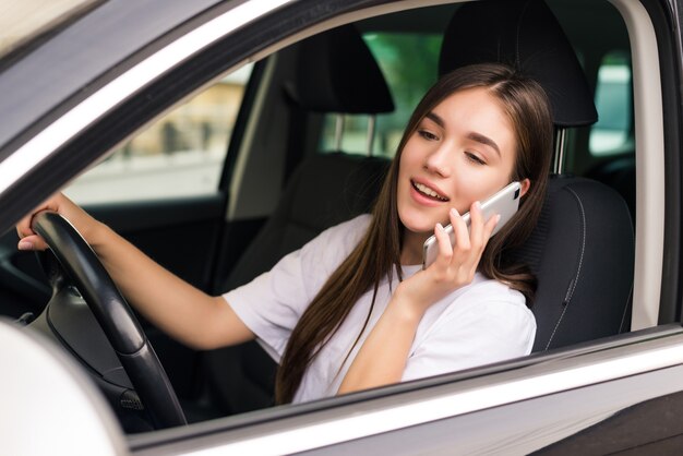 Bella giovane donna seduta in macchina con il computer portatile e parlando al telefono.