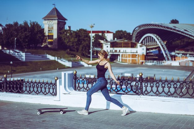 Bella giovane donna skater in sella al suo longboard in città. Ragazza alla moda in abiti da strada cavalca su un longboard.