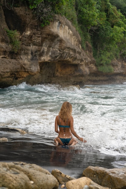 Bella giovane donna snella con lunghi capelli biondi in un costume da bagno sulla spiaggia vicino all'oceano. Rilassatevi sulla spiaggia. Vacanze tropicali.