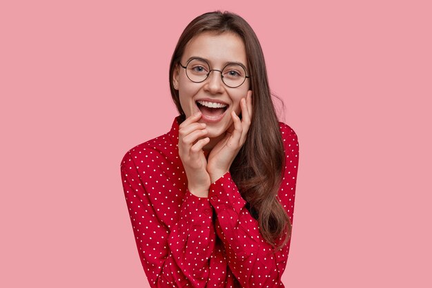 Bella giovane donna sorride positivamente, mostra denti bianchi perfetti, ha una pelle morbida e sana, vestita con una camicia a pois