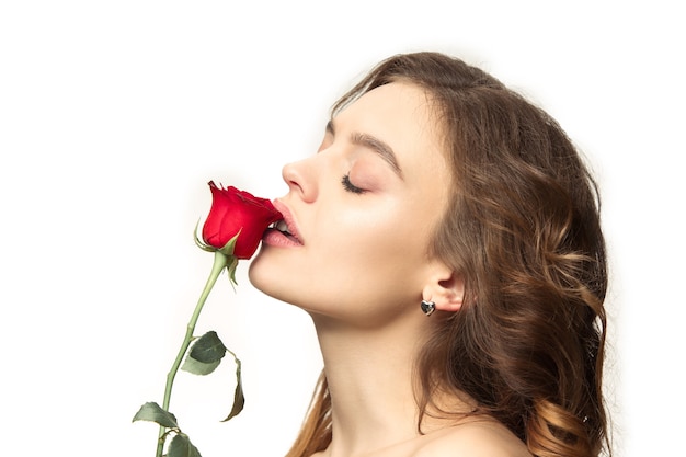 Bella giovane donna sorridente con lunghi capelli setosi ondulati, trucco naturale con rosa rossa isolata su bianco