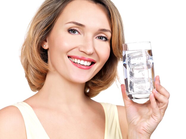 Bella giovane donna sorridente con un bicchiere d'acqua su un muro bianco