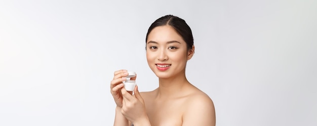 Bella giovane donna su sfondo bianco isolato tenendo la crema viso cosmetica asiatica