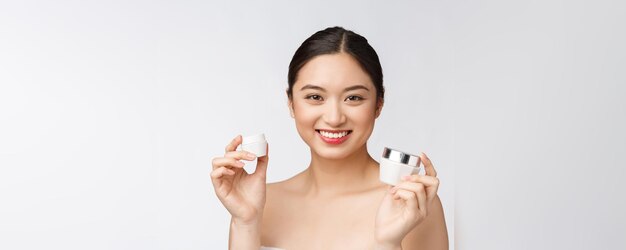 Bella giovane donna su sfondo bianco isolato tenendo la crema viso cosmetica asiatica