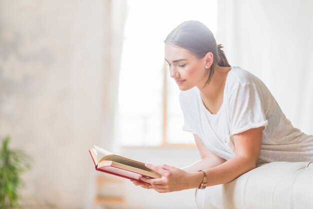 Bella giovane donna sul libro di lettura del letto