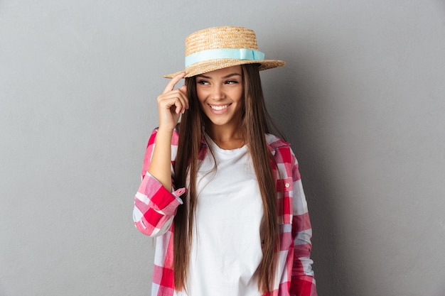 Bella giovane donna, toccando il suo cappello di paglia, guardando lontano