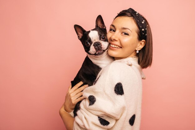 Bella giovane ragazza bruna caucasica coccola bulldog francese su sfondo rosa che mostra il concetto di affetto