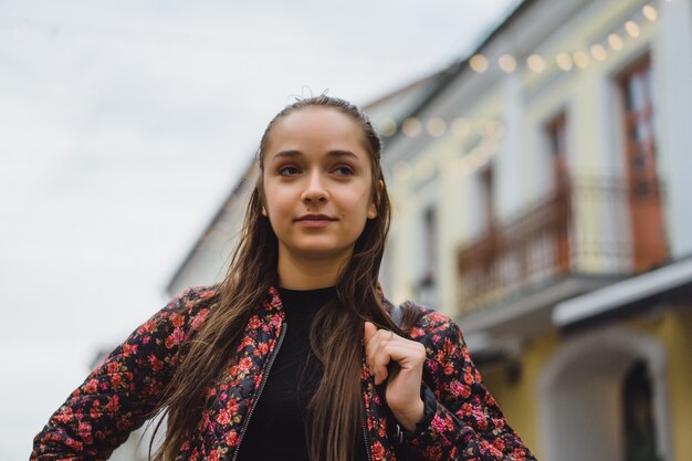 Bella giovane ragazza bruna felice con i capelli lunghi che propongono all&#39;aperto. Foto di strada, ritratto, primo piano.