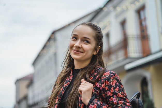 Bella giovane ragazza bruna felice con i capelli lunghi che propongono all&#39;aperto. Foto di strada, ritratto, primo piano.