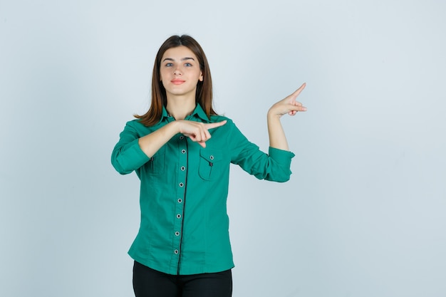 Bella giovane signora che indica a destra in camicia verde e che sembra sicura. vista frontale.