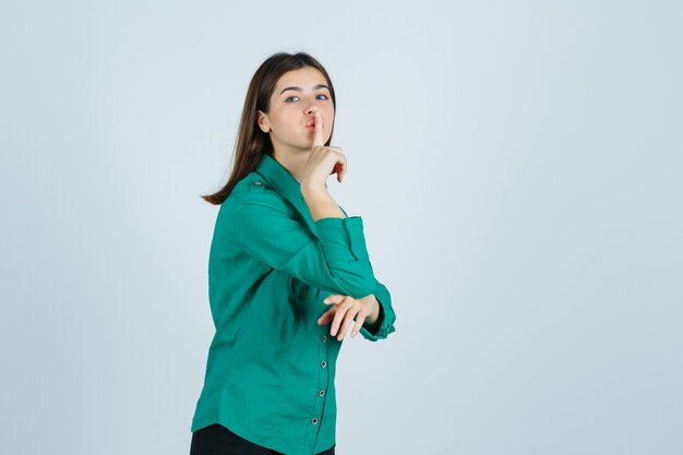 Bella giovane signora che mostra gesto di silenzio in camicia verde e guardando attento. vista frontale.