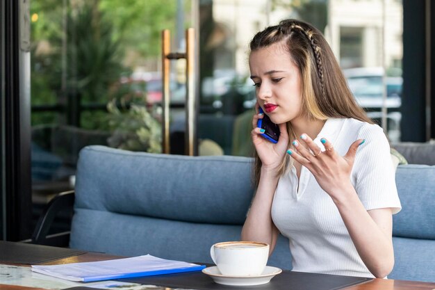 Bella giovane signora che si sente arrabbiata e parla al telefono al ristorante