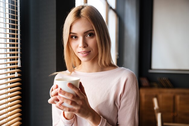 Bella giovane signora che sta nel caffè bevente del caffè