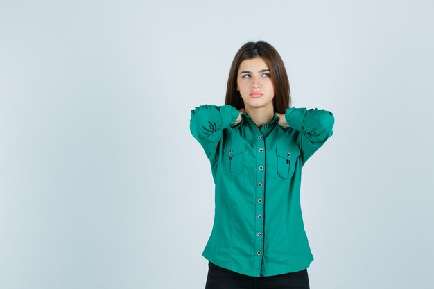 Bella giovane signora che tiene le mani sul collo in camicia verde e guardando abbattuto, vista frontale.