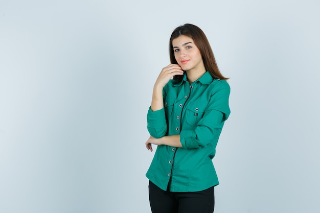 Bella giovane signora in camicia verde che tocca il mento con la mano e che sembra delicata, vista frontale.