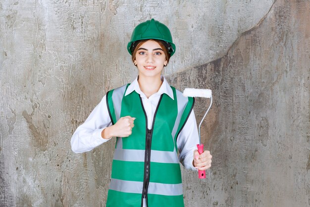 Bella lavoratrice edile con rullo di pittura in piedi