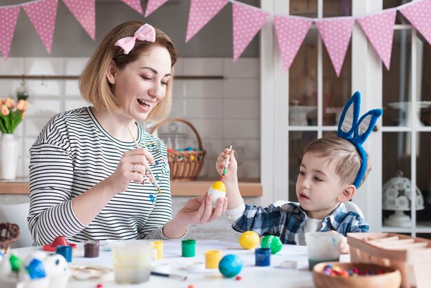 Bella madre che insegna al ragazzino sveglio come dipingere le uova