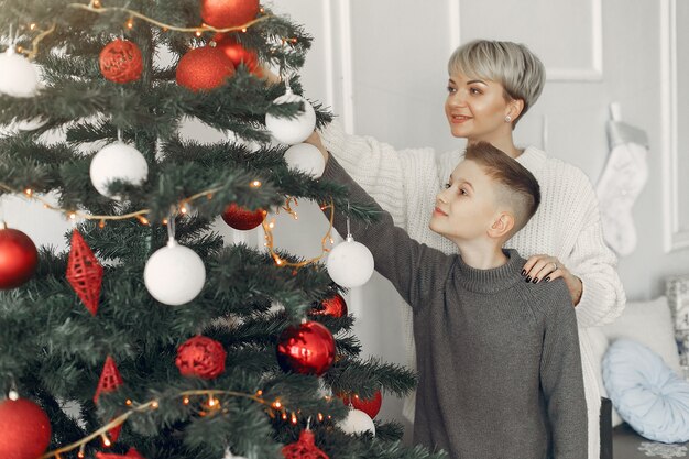 Bella madre in un maglione bianco. Famiglia in decorazioni natalizie. Ragazzino in una stanza